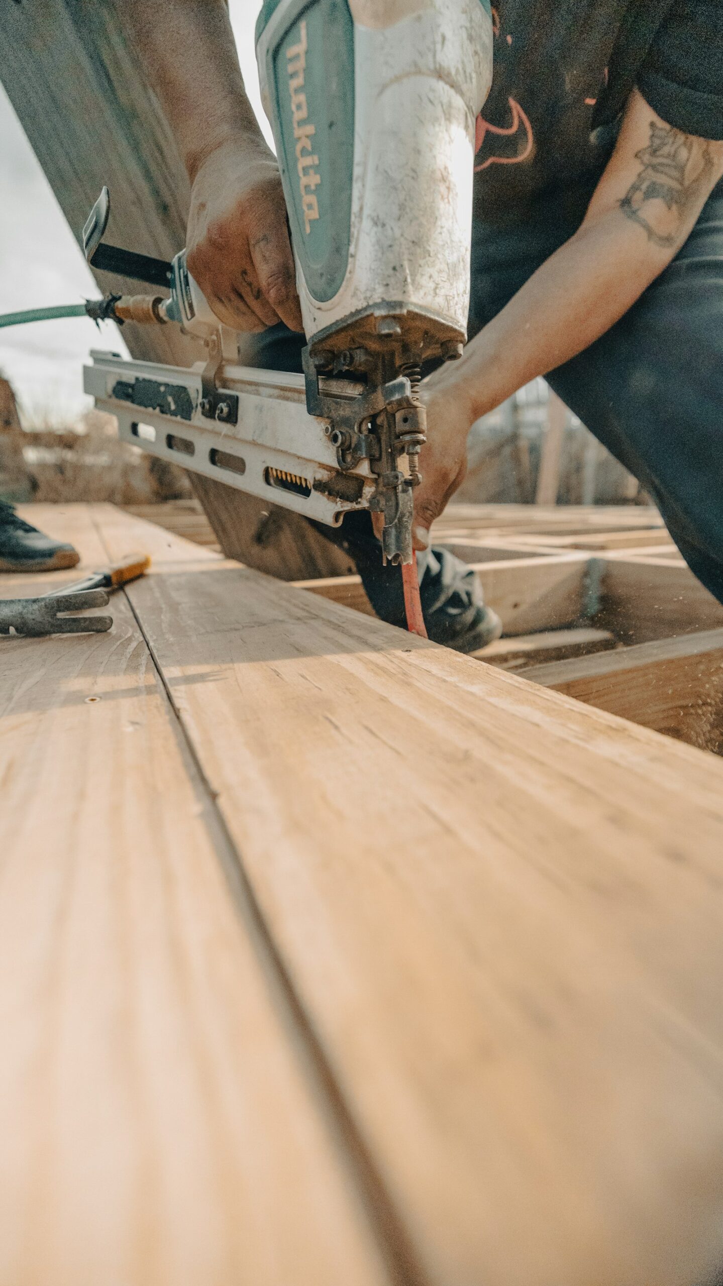 Pose de lames de terrasse en bois à la cloueuse pneumatique par un artisan